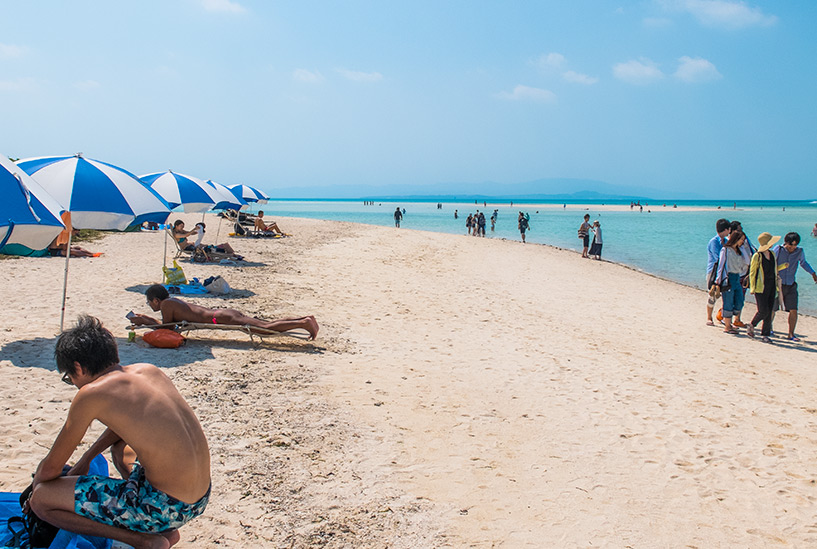 Plage à parasols et quinquagénaire japonais en moule-bite rose fluo, Taketomi-jima